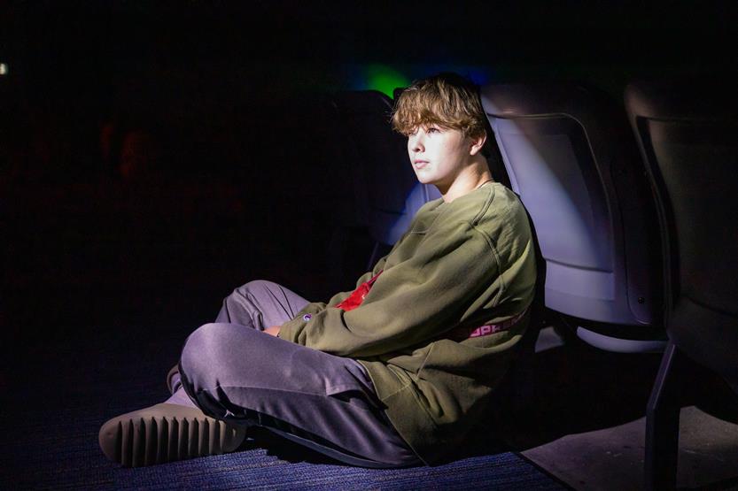 A boy sits on the ground while a light shines on him